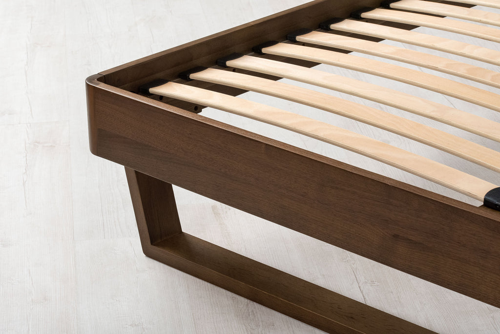 Mayfair solid walnut double bed frame foot-end corner close-up, showing the rounded corner, sprung slats and floating sled leg