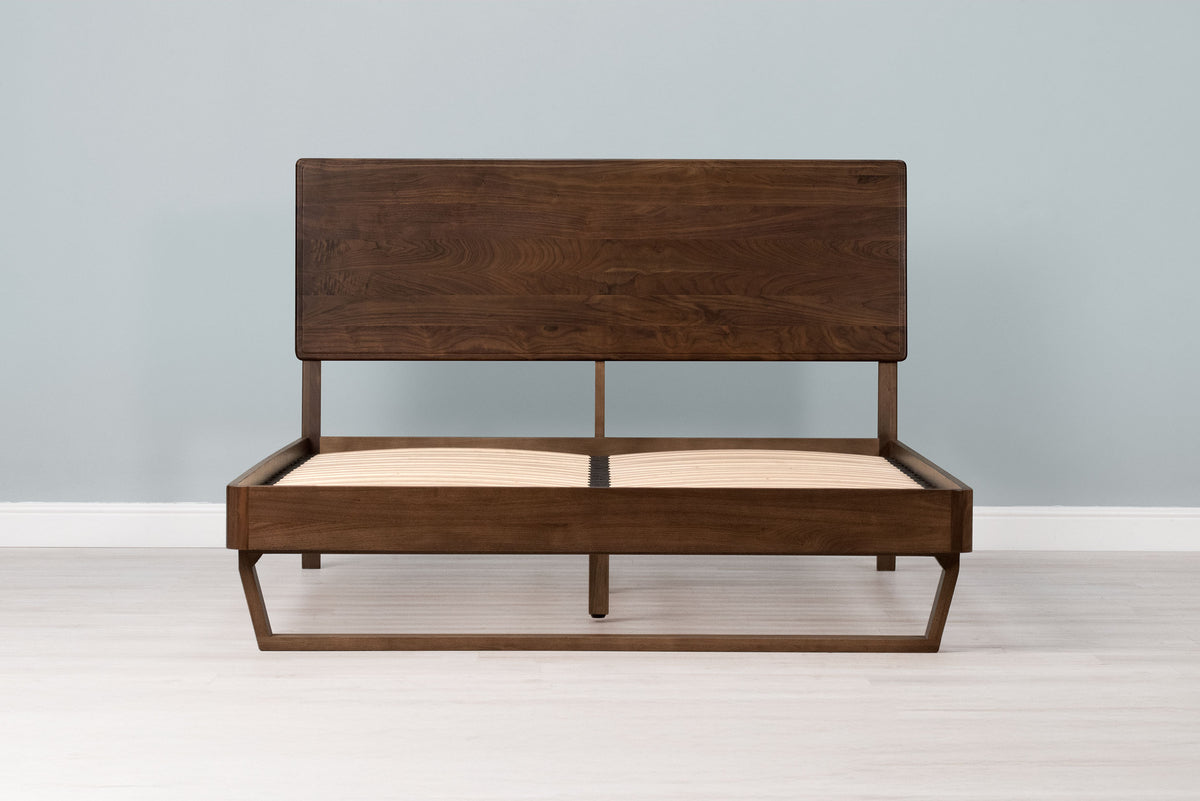 Mayfair solid walnut double bed frame with floating sled leg and no mattress, front view from the foot of the bed
