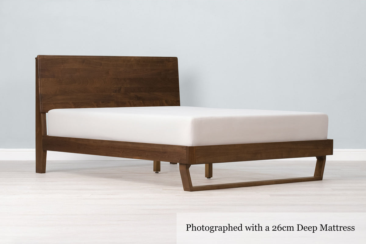 Mayfair solid walnut double bed frame with floating sled leg, a 26cm deep mattress and no bedding, angled view