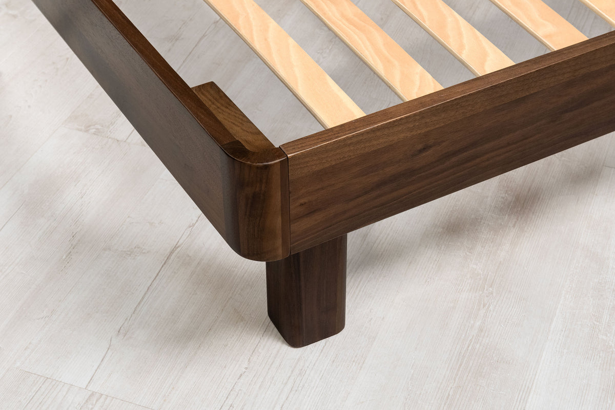Mayfair solid walnut double bed frame foot-end close-up, showing the rounded corner and chunky 8cm square walnut leg
