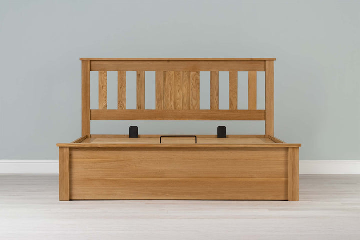 Wilmore solid natural oak double ottoman bed frame without a mattress, front view from the foot of the bed