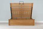 Wilmore solid natural oak double ottoman bed frame without a mattress, front view with the slatted base fully raised