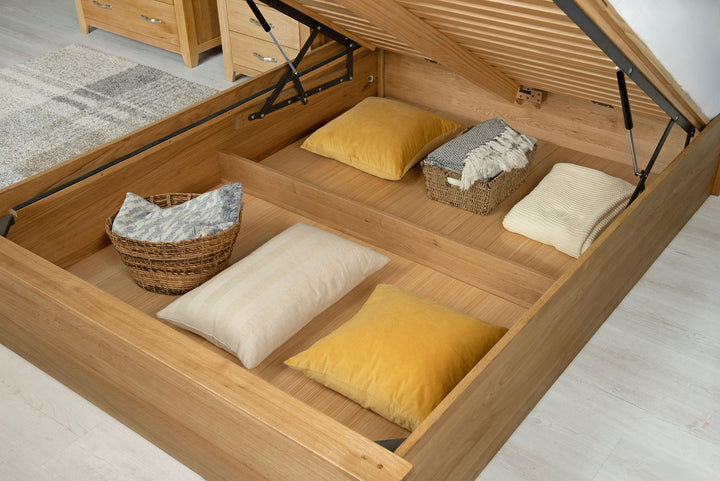 Wilmore solid natural oak double ottoman bed storage area holding cushions, pillows and baskets on the removable base panels