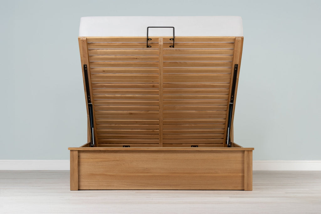 Wilmore solid natural oak king size ottoman bed frame with a bare mattress and the base raised, front view from the foot of the bed