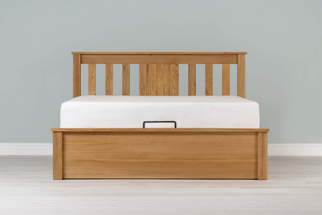Wilmore solid natural oak super king ottoman bed frame with a bare mattress and no bedding, front view from the foot of the bed