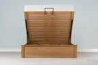Wilmore solid natural oak super king ottoman bed frame with a bare mattress and the base raised, front view from the foot of the bed
