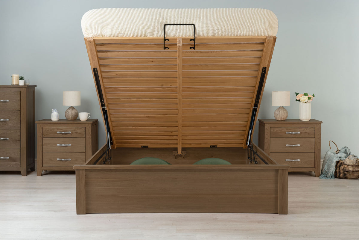 Wilmore solid rustic oak super king ottoman bed frame with the mattress base raised, front view showing the under-bed storage in a dressed bedroom