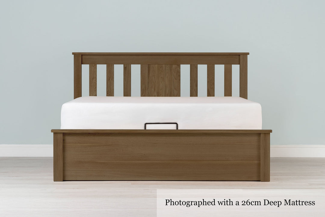 Wilmore solid rustic oak super king ottoman bed frame with a 26cm deep mattress and no bedding, front view from the foot of the bed