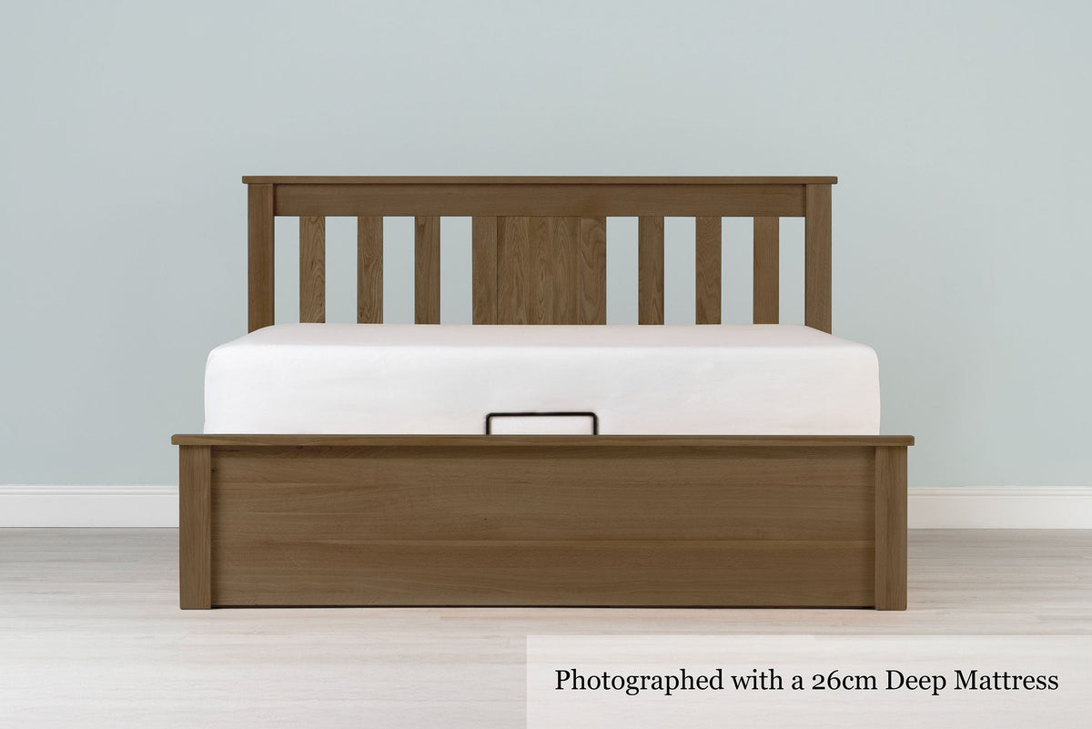 Wilmore solid rustic oak super king ottoman bed frame with a 26cm deep mattress and no bedding, front view from the foot of the bed