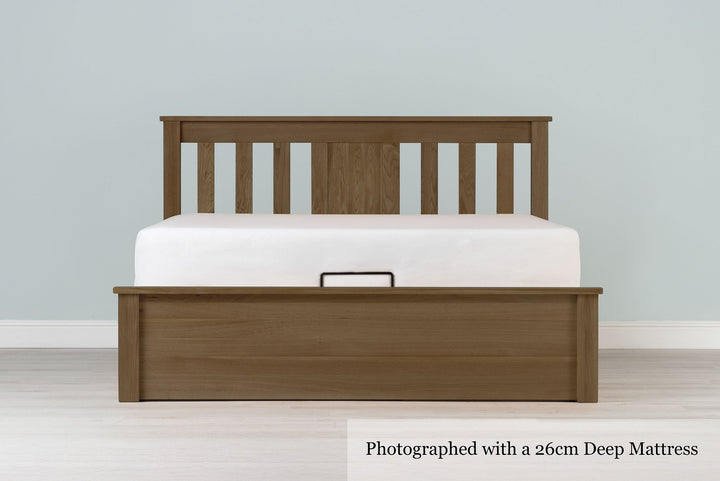 Wilmore solid rustic oak super king ottoman bed frame with a 26cm deep mattress and no bedding, front view from the foot of the bed