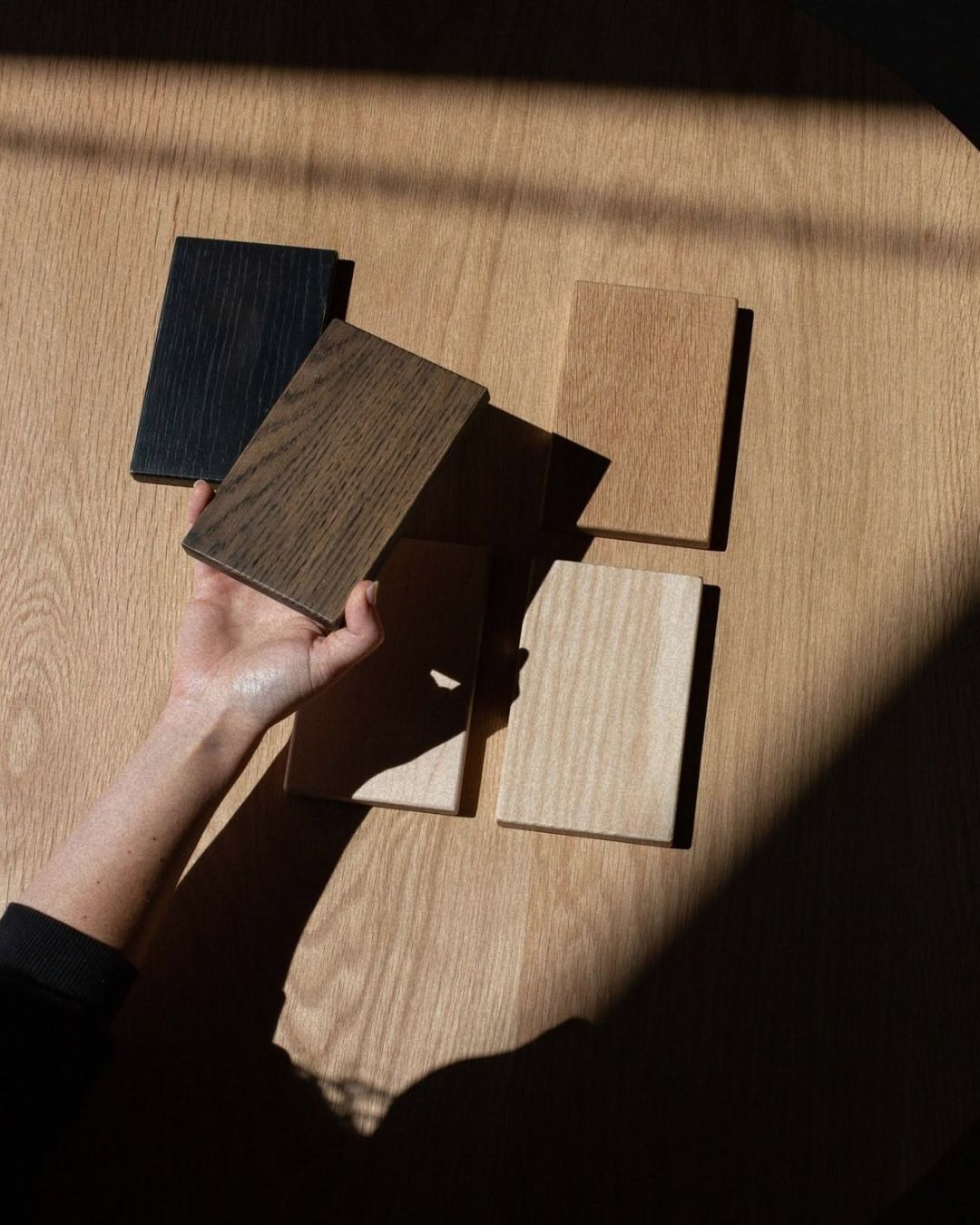 A hand holding solid oak samples in different finishes on a wooden table